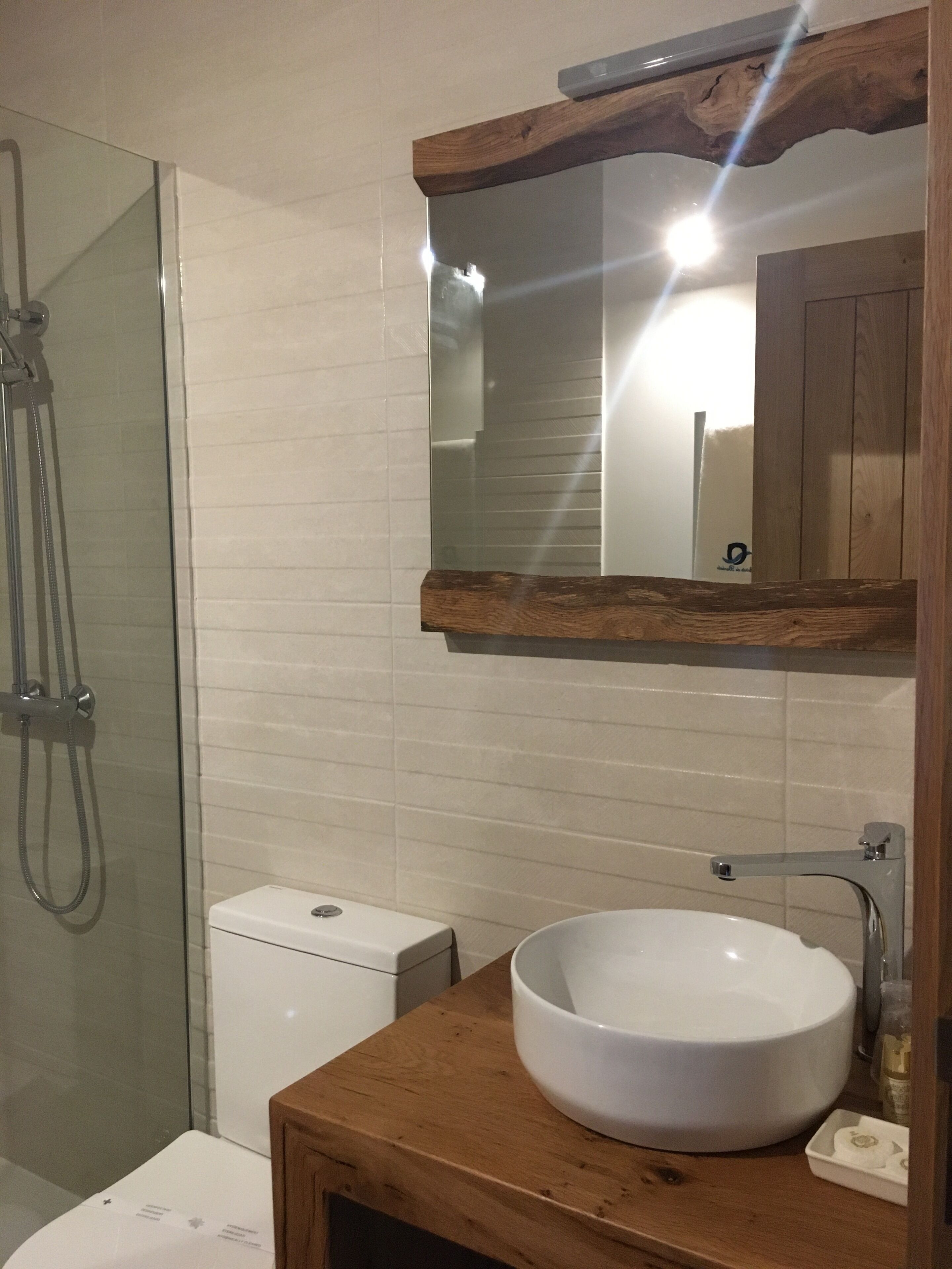 A bathroom with a glass shower enclosure, a white toilet, and a wooden vanity with a large white sink.