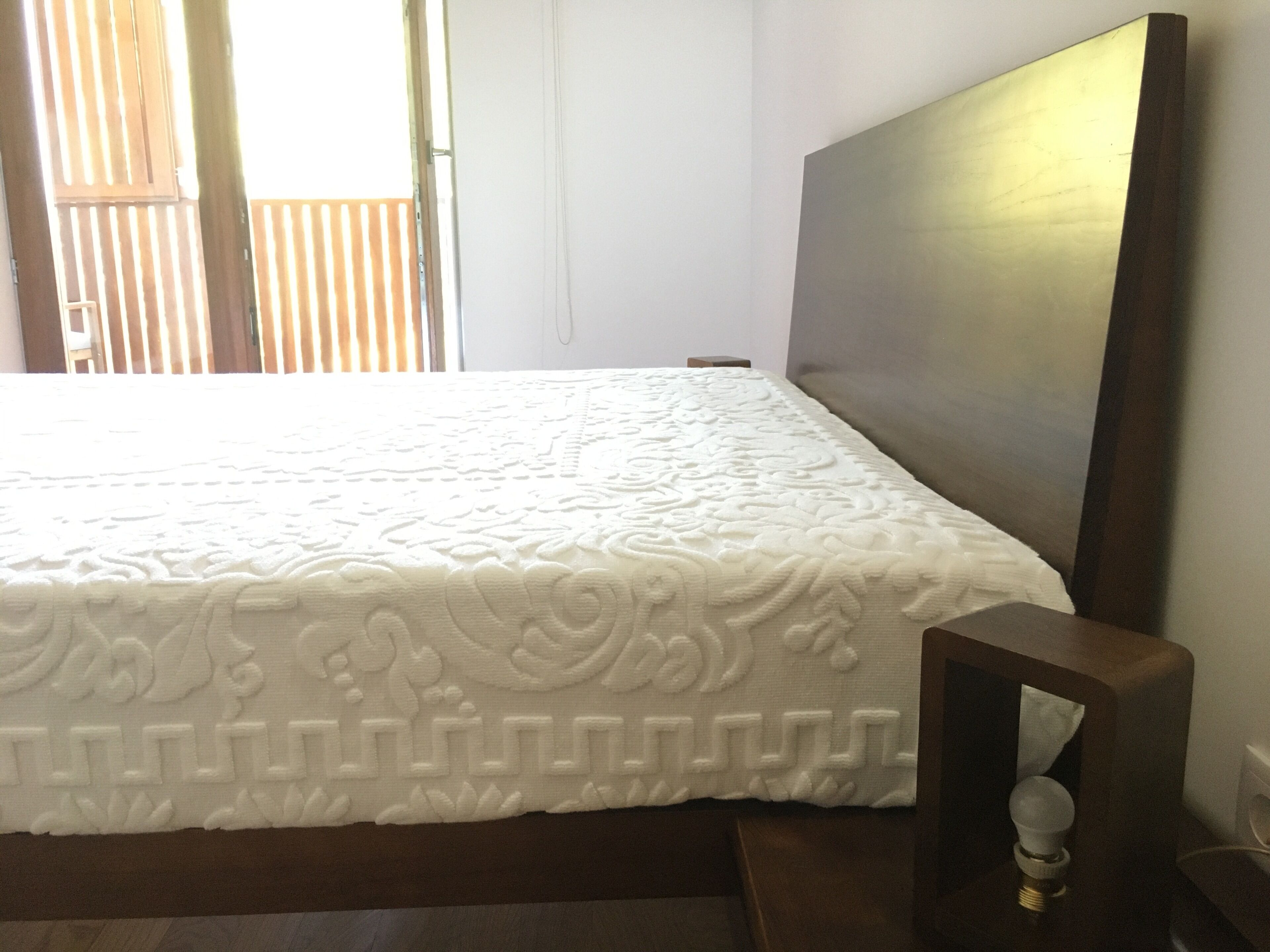 A neatly made bed with a patterned bedspread, a wooden headboard, and a bedside table with a lamp.