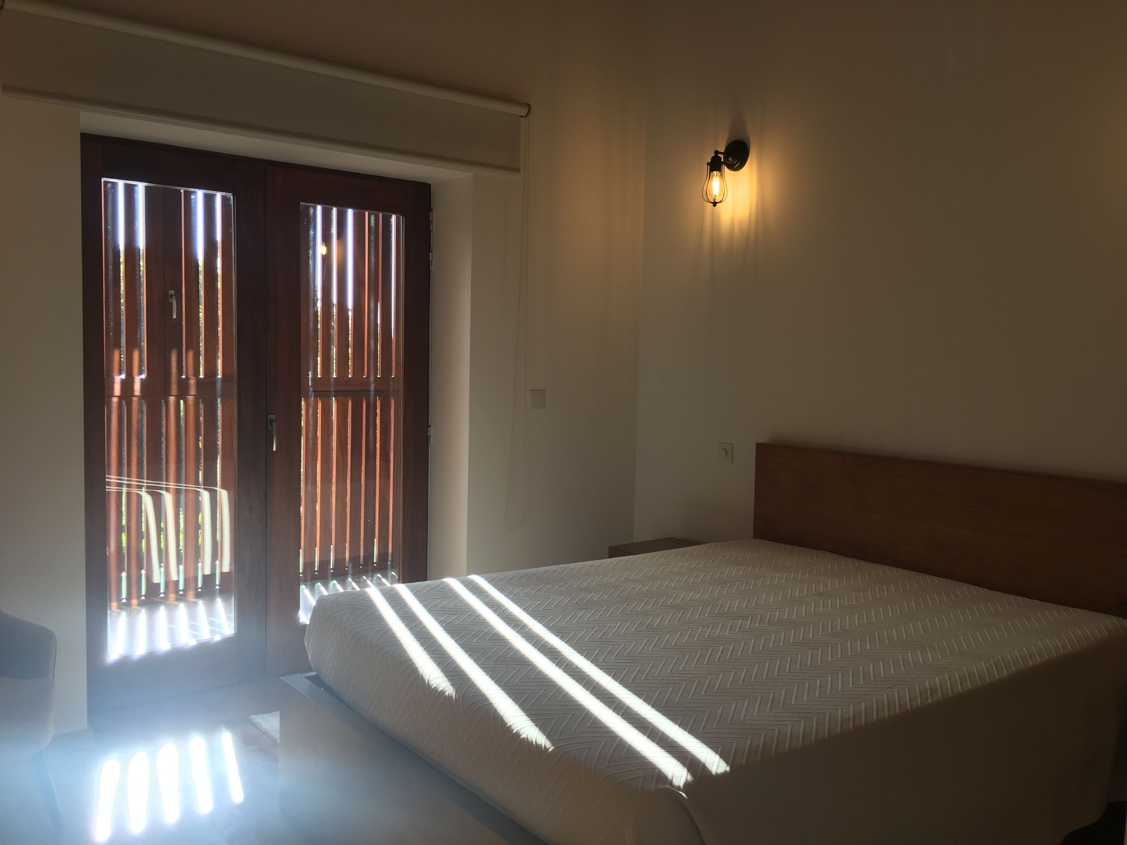 Una camera da letto con un letto, una lampada a parete e una porta scorrevole con persiane verticali.