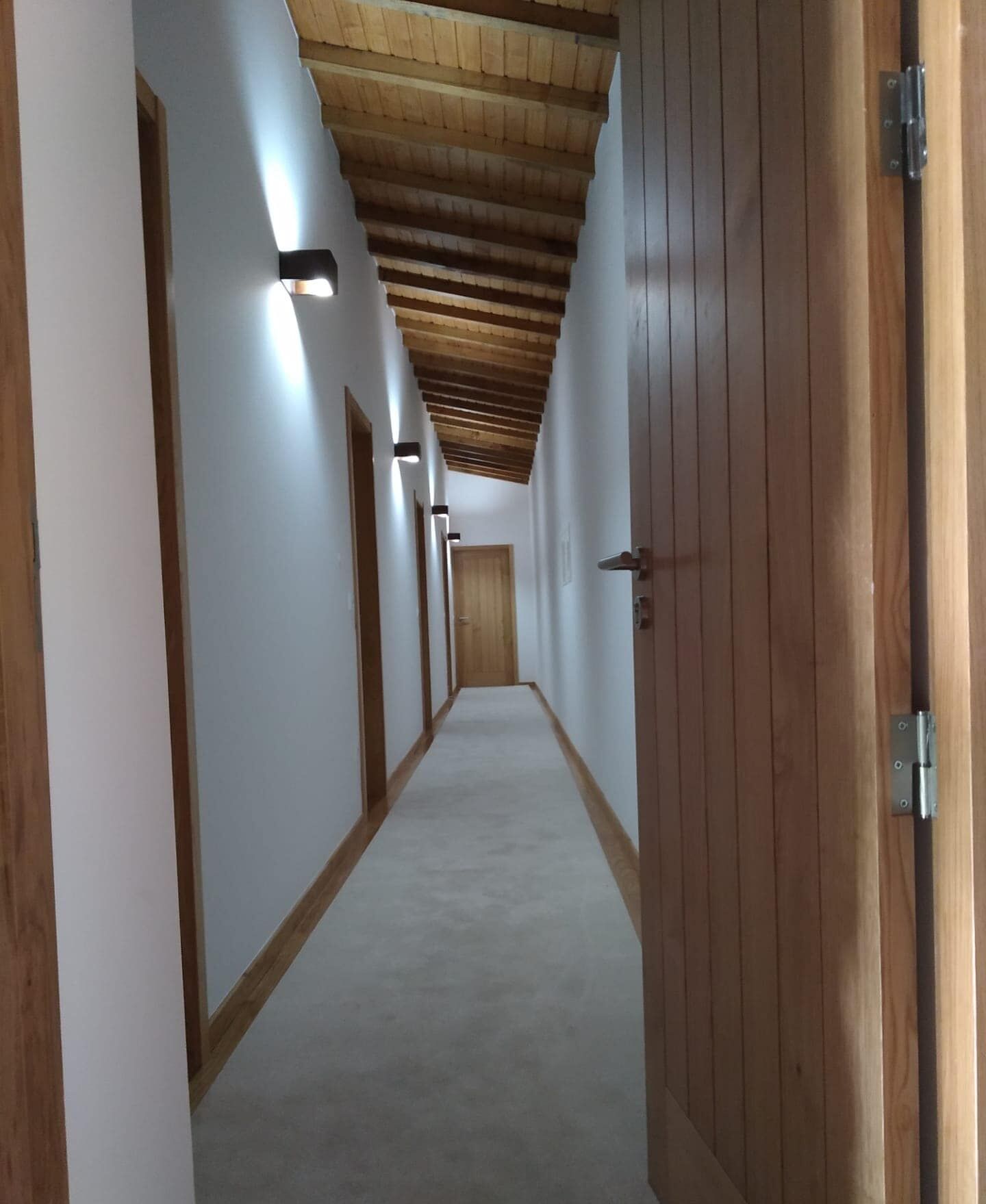 A long, narrow hallway with wooden ceiling beams and white walls.