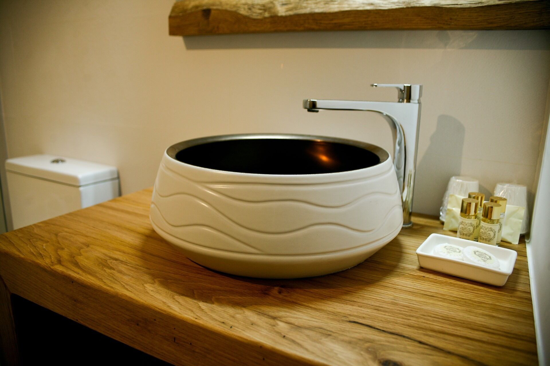 A bathroom with a wooden vanity, a white ceramic sink with a wavy design, and a small white soap dish with bottles.