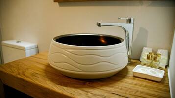 A bathroom with a wooden vanity, a white ceramic sink with a wavy design, and a small white soap dish with bottles.
