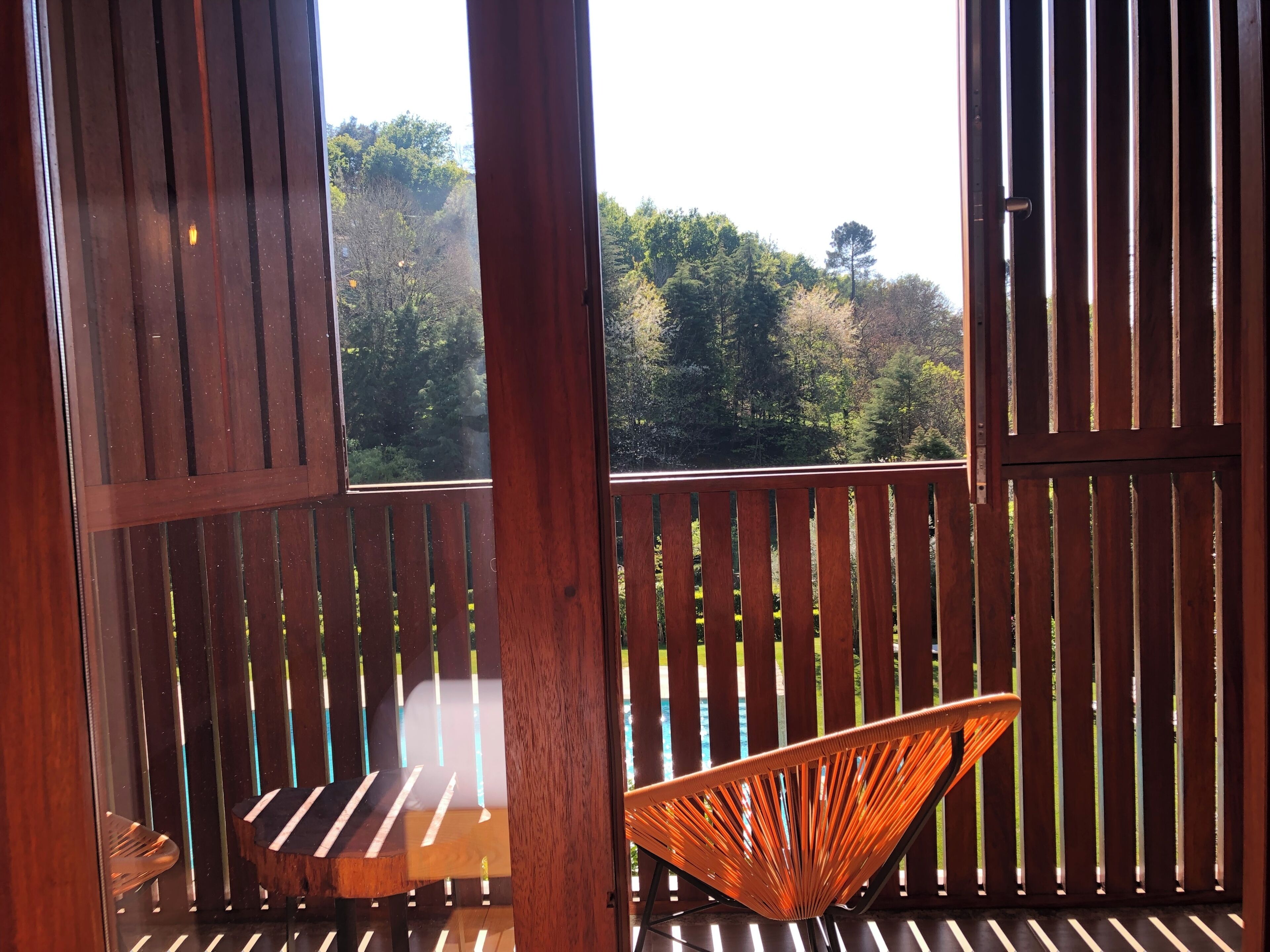 A wooden deck with a wooden chair and a bench, overlooking a forested area.
