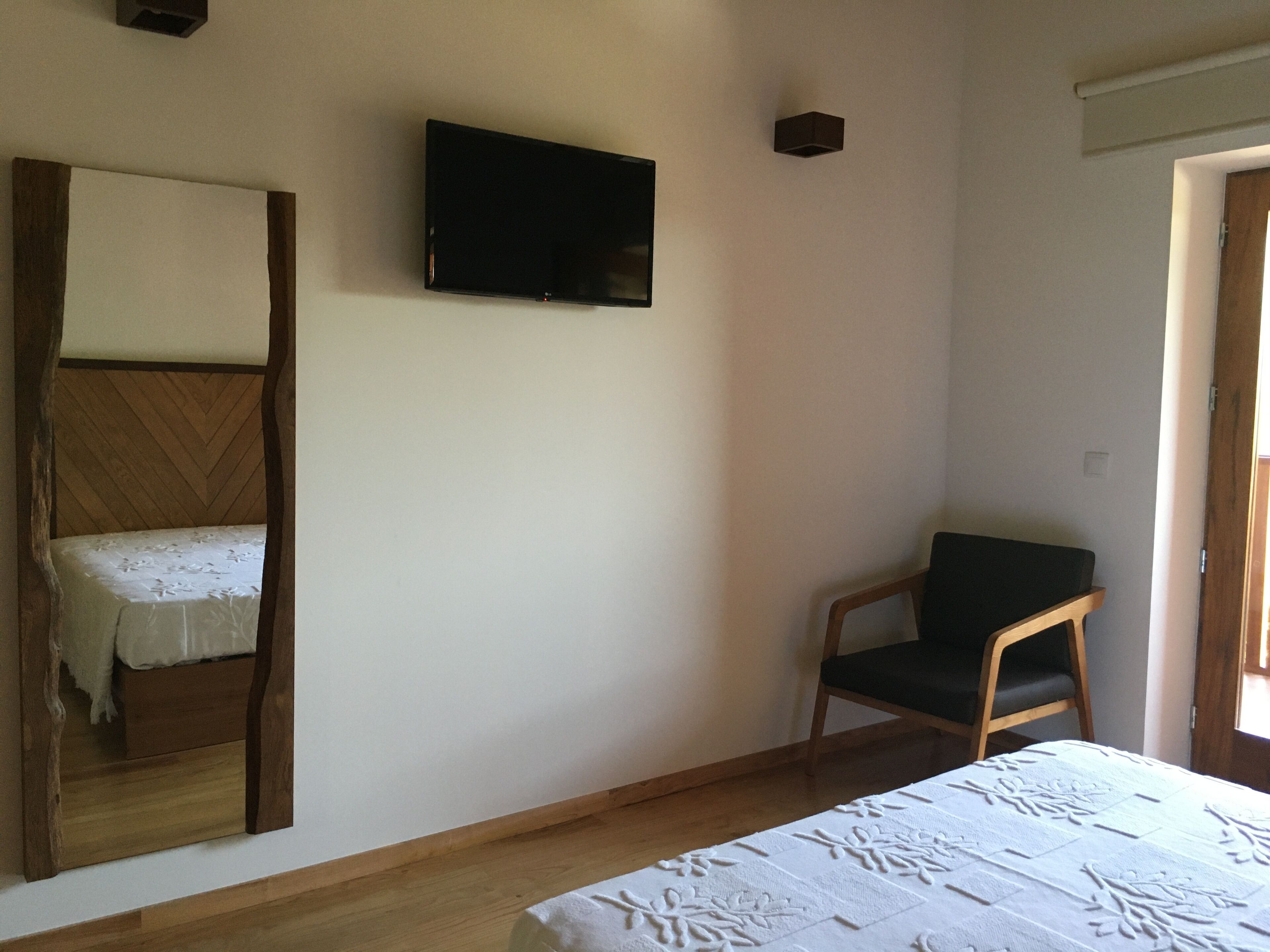 A room with a bed, a chair, a television mounted on the wall, and a wooden headboard.