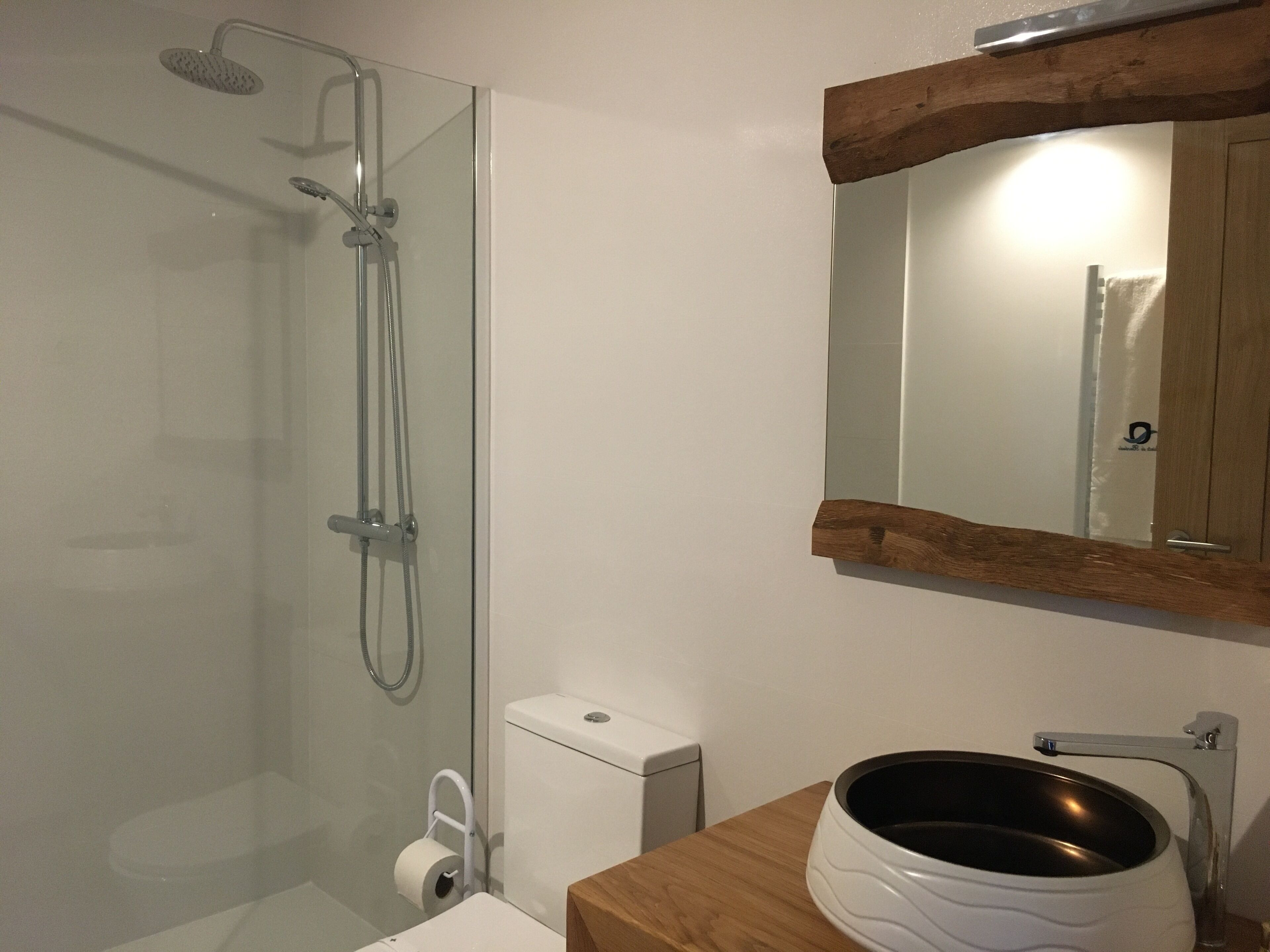 Un baño moderno con ducha de vidrio, inodoro blanco y tocador de madera con lavamanos.