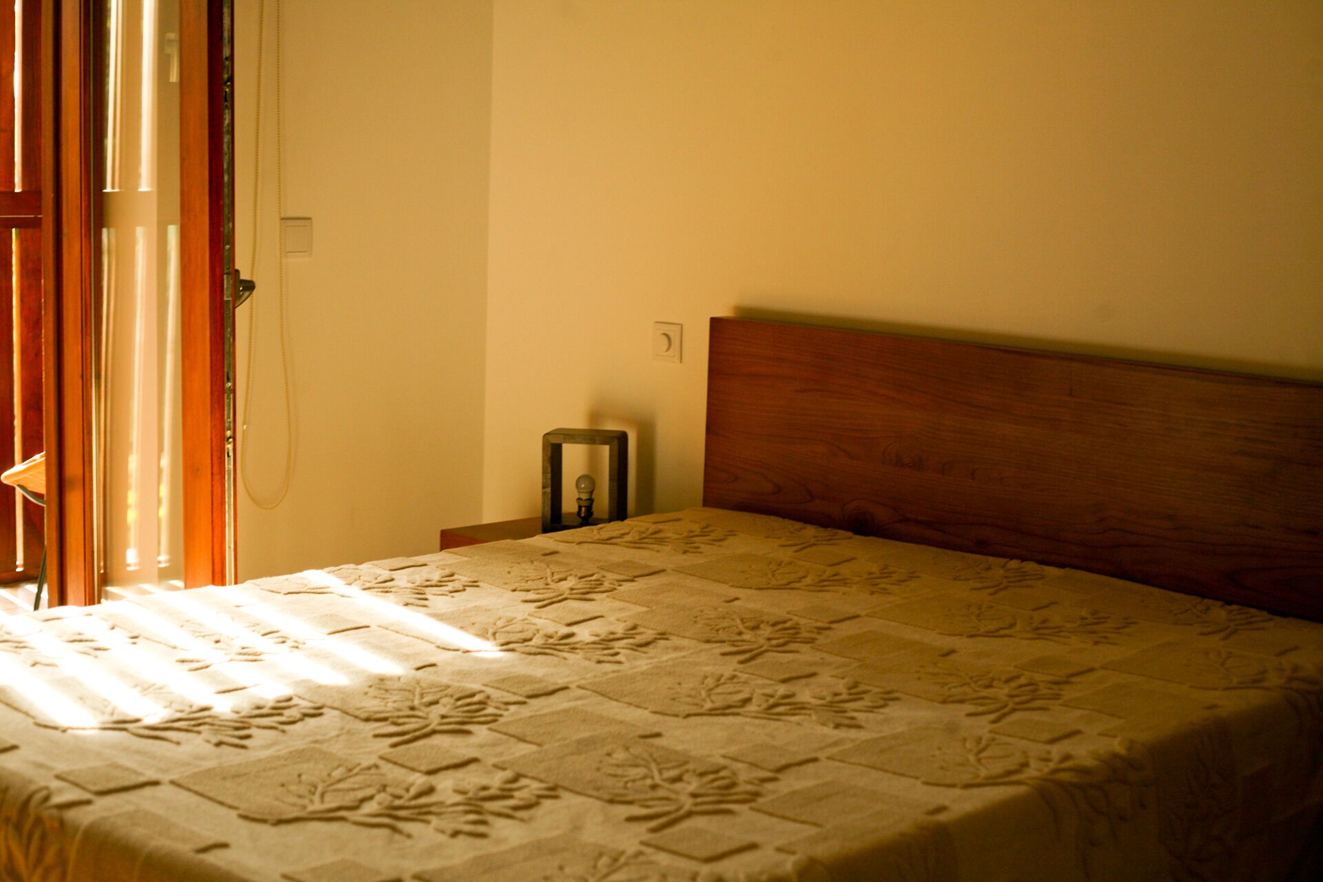 A bedroom with a wooden headboard, a bed with a patterned bedspread, a bedside table, and a nightstand.