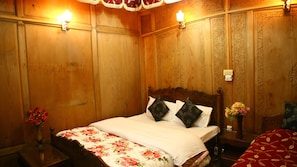 Quarto com painéis de madeira, uma cama, colcha florida e duas luminárias fixadas na parede.