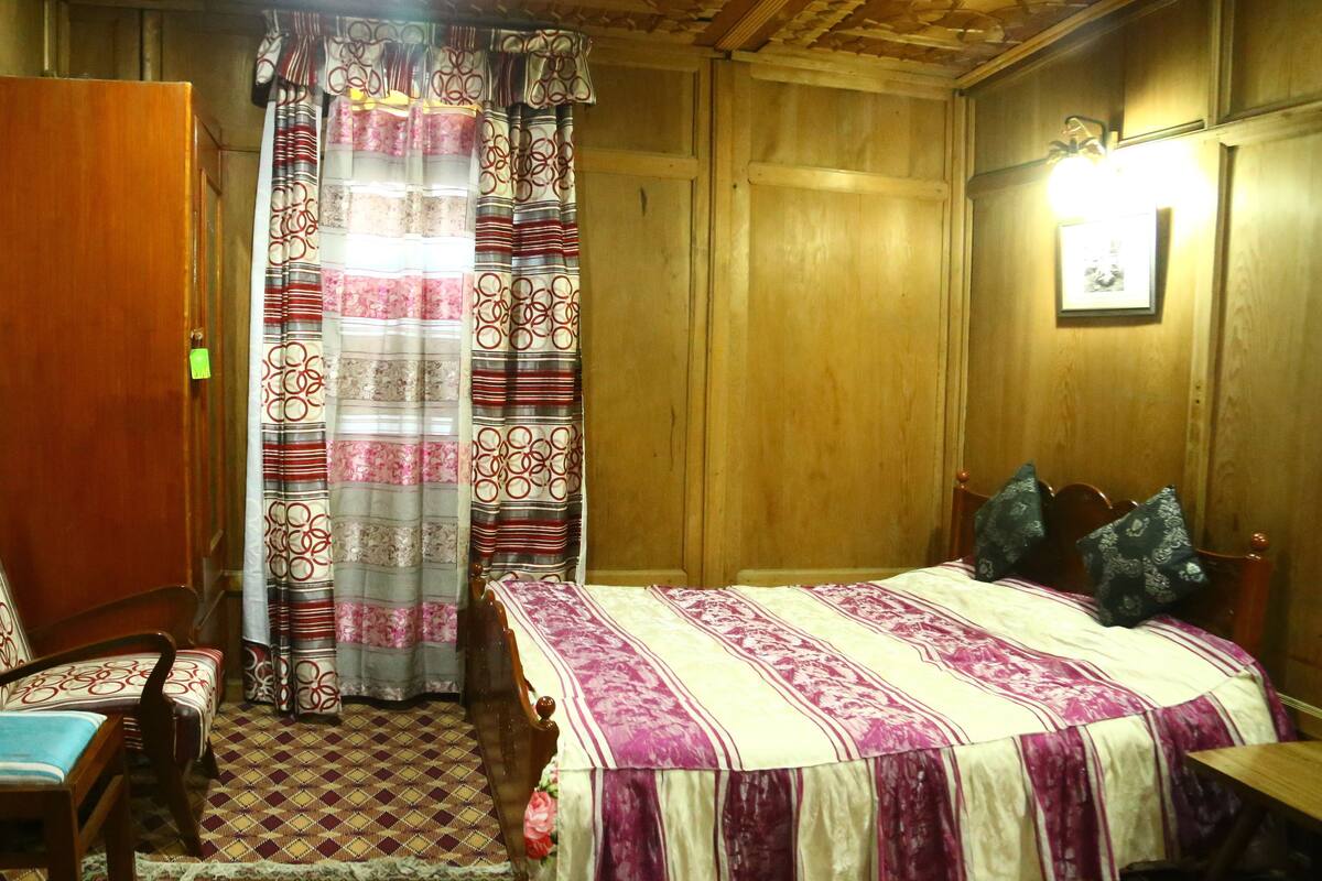 A wooden-paneled room with a bed, a chair, a small table, and a curtain with a circular pattern.