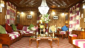 A traditional room with ornate wooden paneling, a chandelier, and a sofa set with cushions. - Aziz Palace (Srinagar)