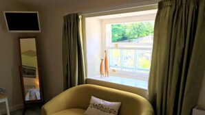 A yellow sofa with a decorative pillow, a flat-screen TV mounted on the wall, and a window with curtains.