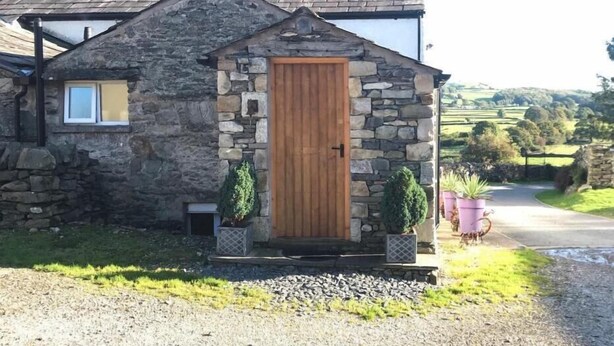 A stone cottage with a wooden door, a small window, and two potted plants.