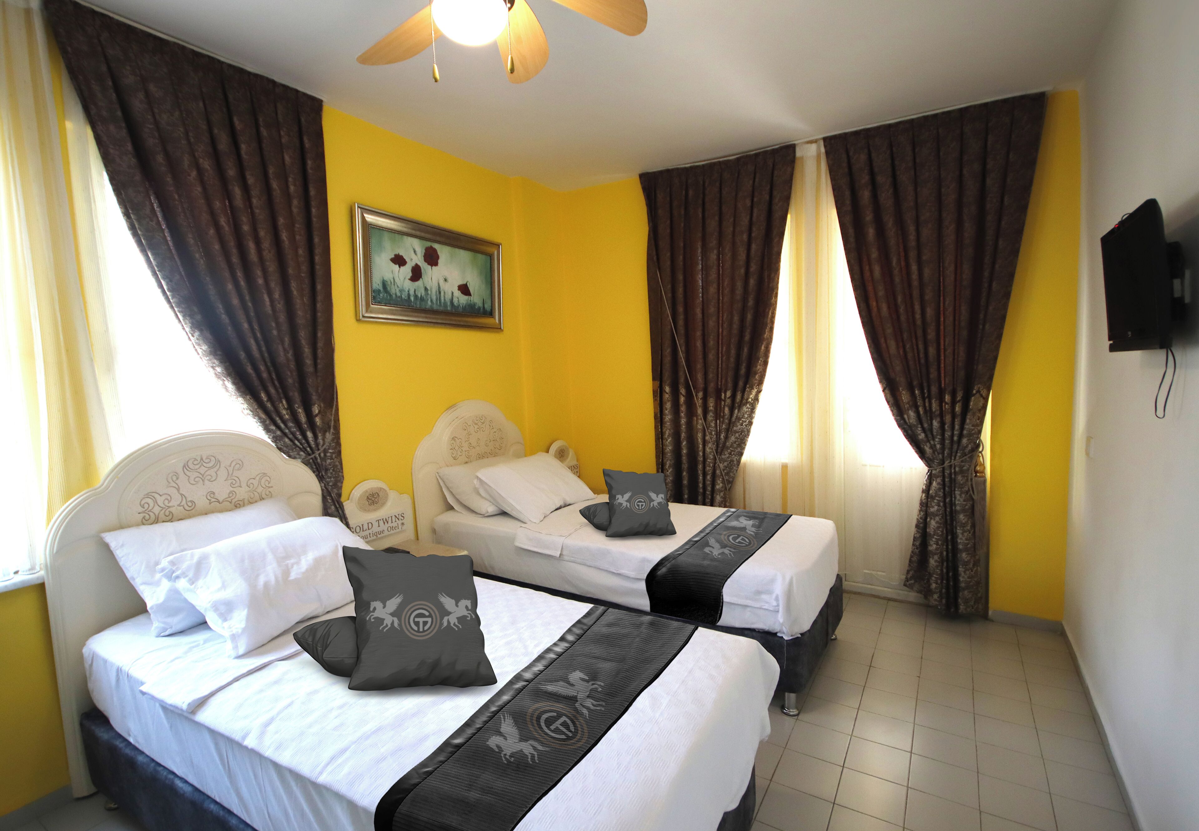 A room with two beds, a ceiling fan, a painting, and curtains.