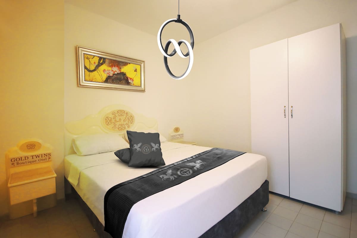 Ein Hotelzimmer mit Bett, Schrank, Nachttisch, einem gerahmten Bild und einer ungewöhnlichen, runden Leuchte.