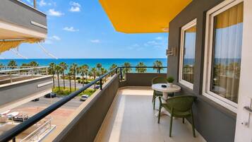 A balcony with a view of the ocean, a table with chairs, and a small potted plant.