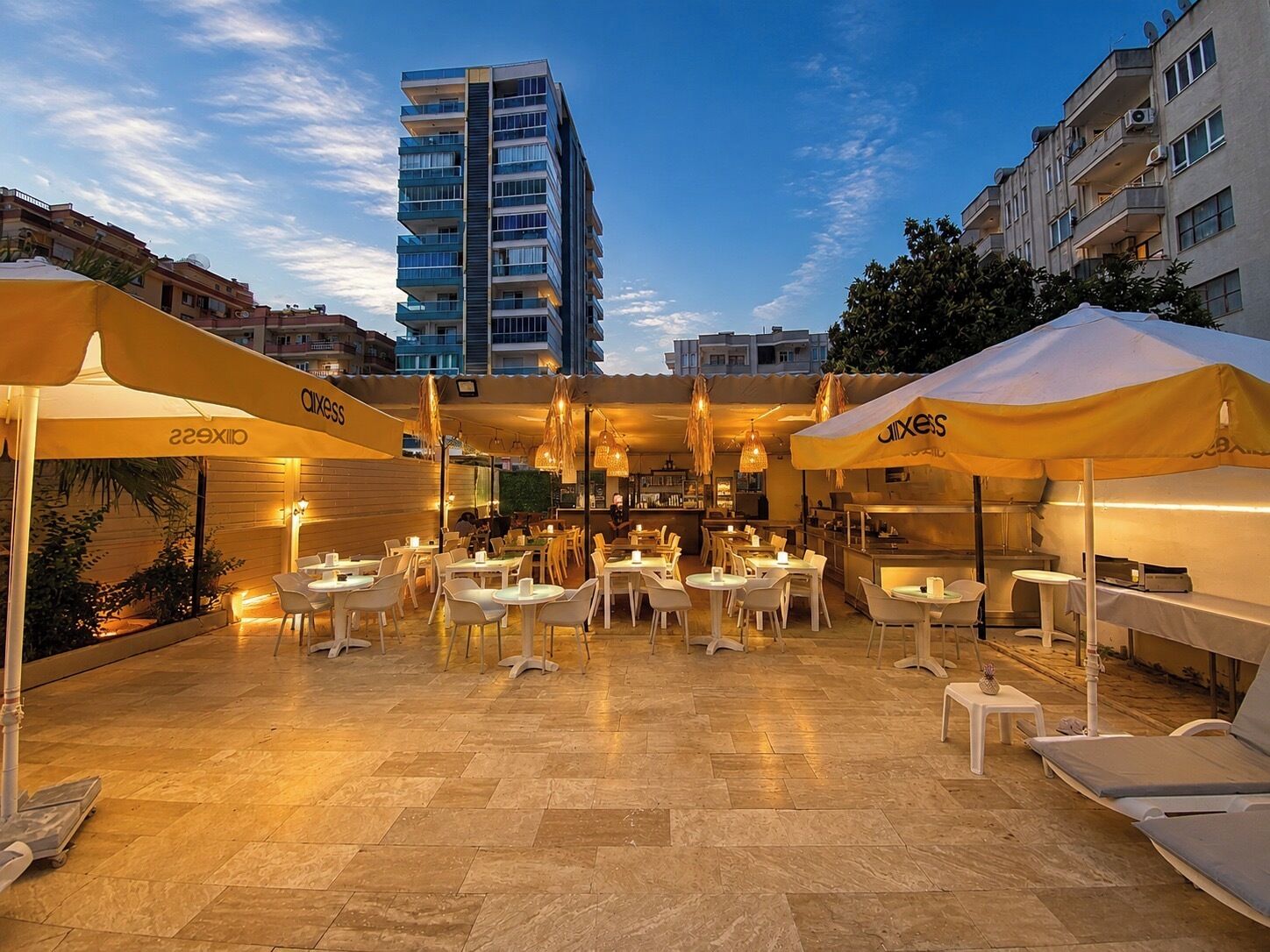 An outdoor dining area with tables and chairs, umbrellas, and a view of a tall building in the background.