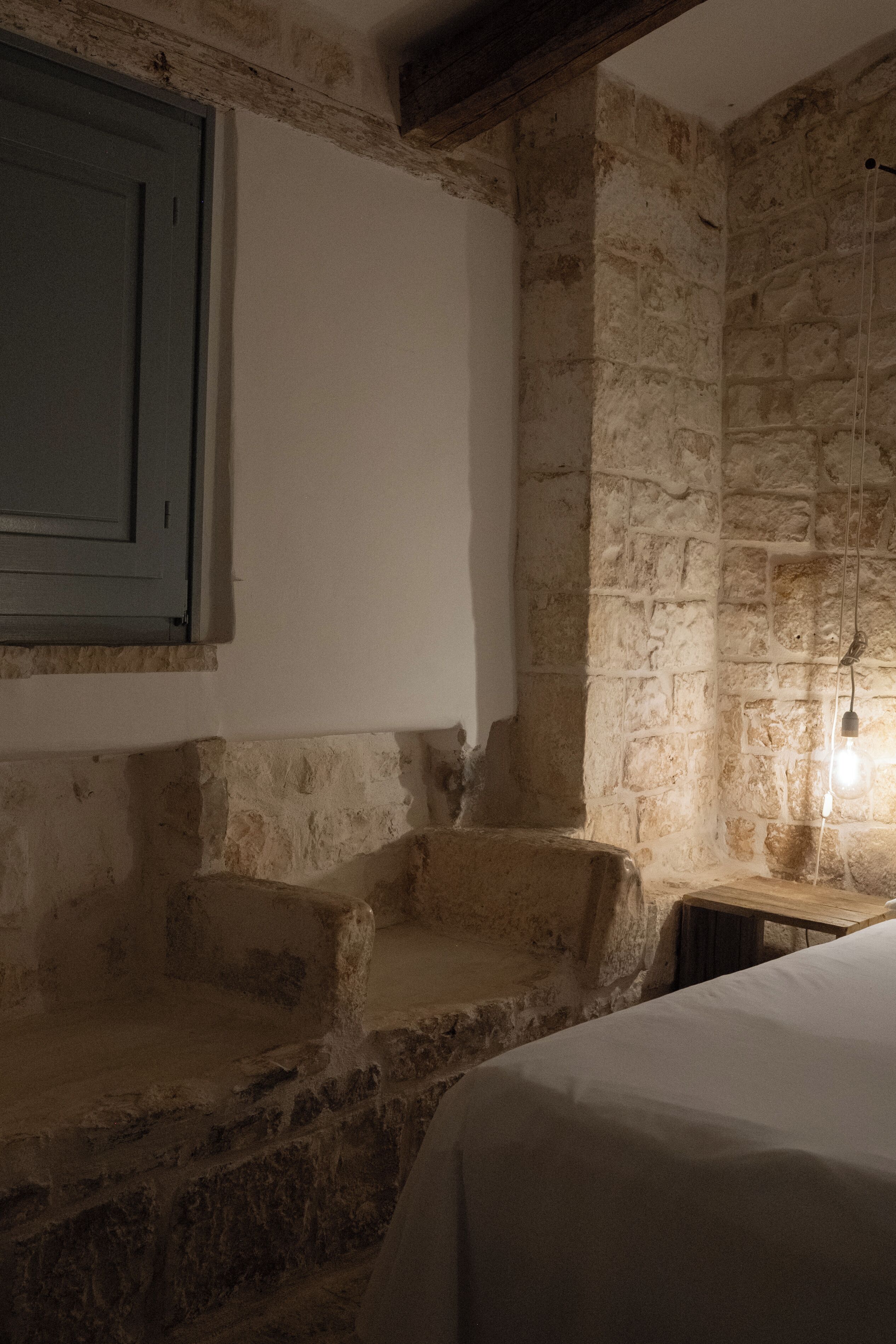 Una habitación rústica con paredes de piedra, una escalera de madera, una cama y una lámpara colgante.