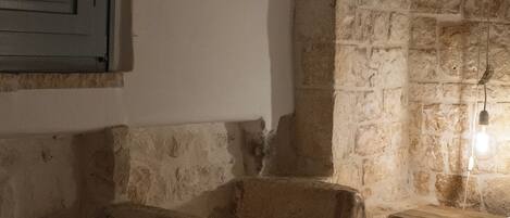Una habitación rústica con paredes de piedra, una escalera de madera, una cama y una lámpara colgante.