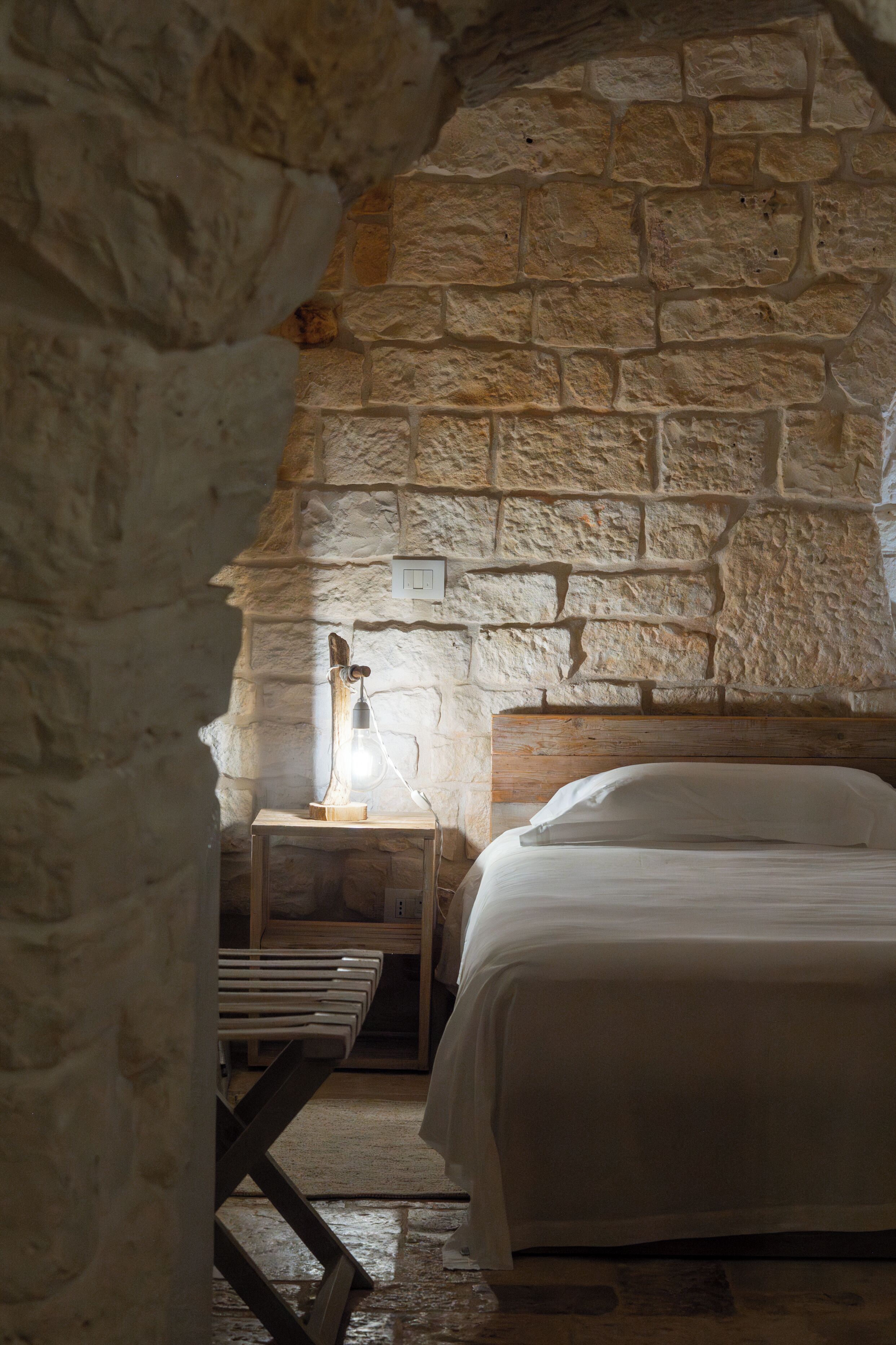 Una stanza con pareti in pietra, un letto, un comodino di legno e un tavolo.