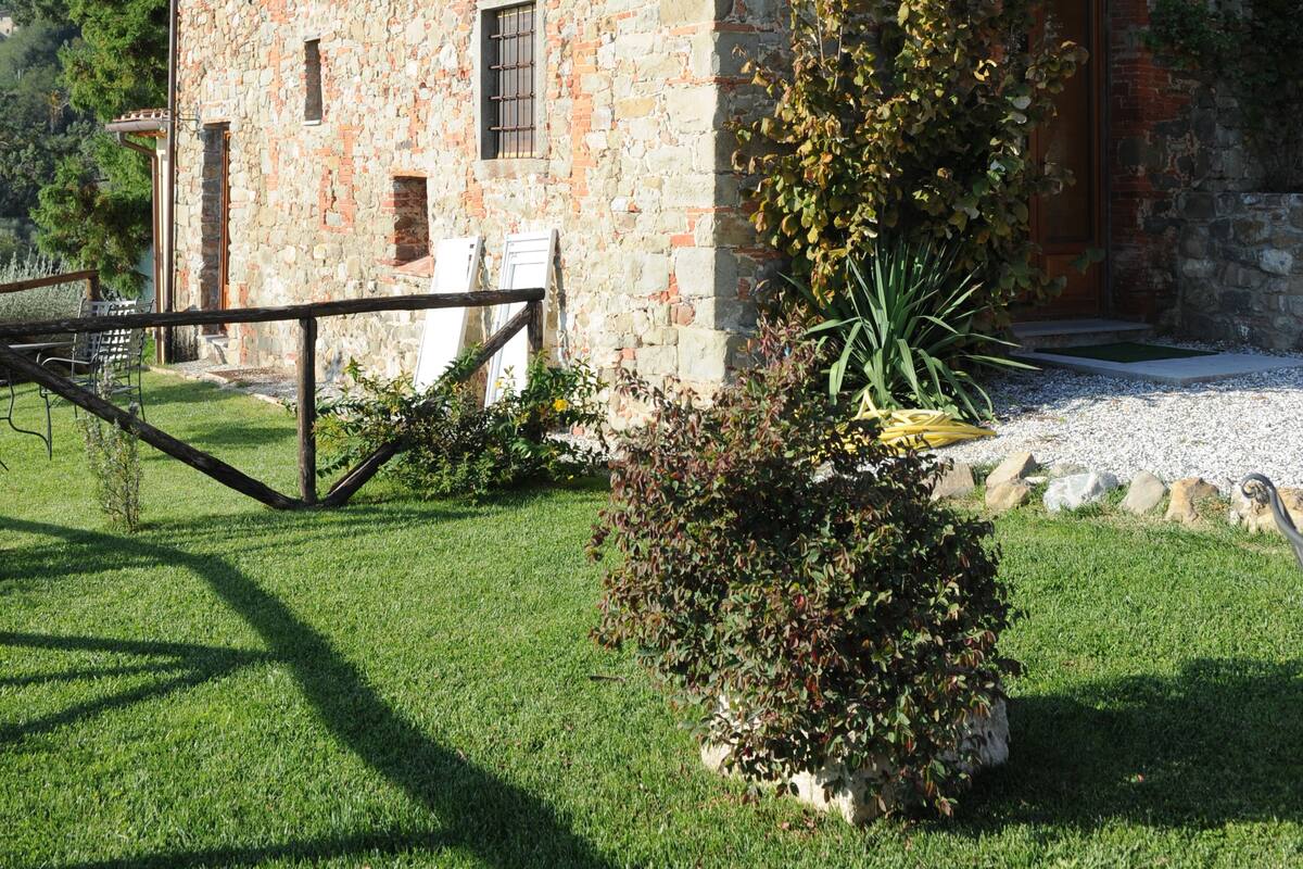 Un edificio de piedra con un balcón de madera, un pequeño jardín y un sendero de grava.