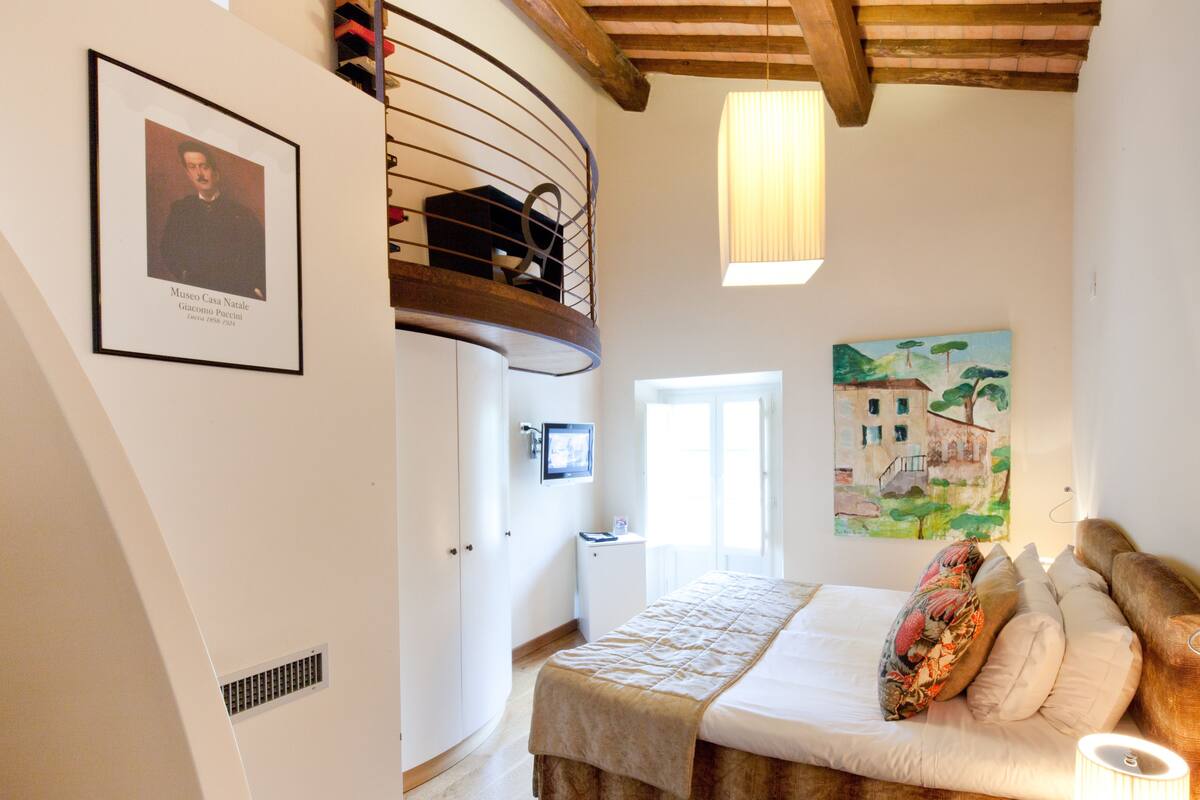 Un dormitorio con una cama, un cuadro, una fotografía enmarco y una escalera.