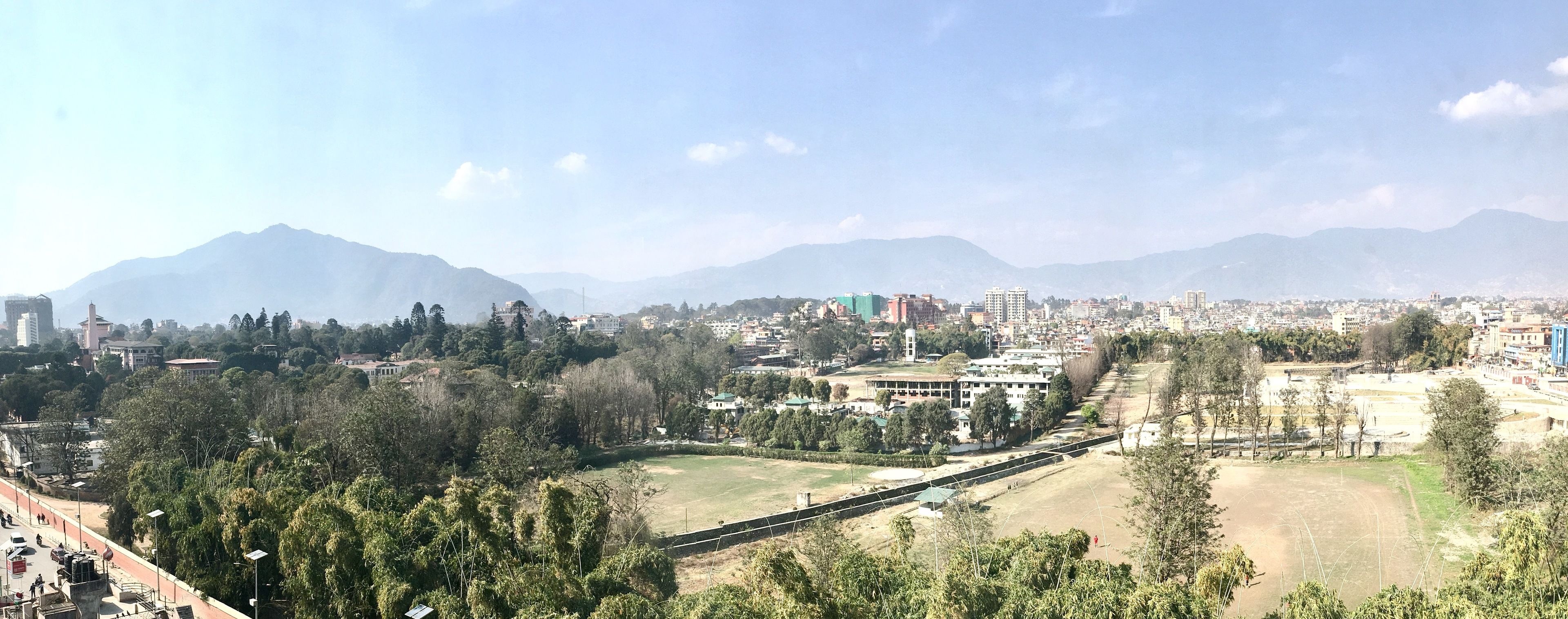 A cityscape with a prominent building with a green roof, surrounded by trees and a clear sky.