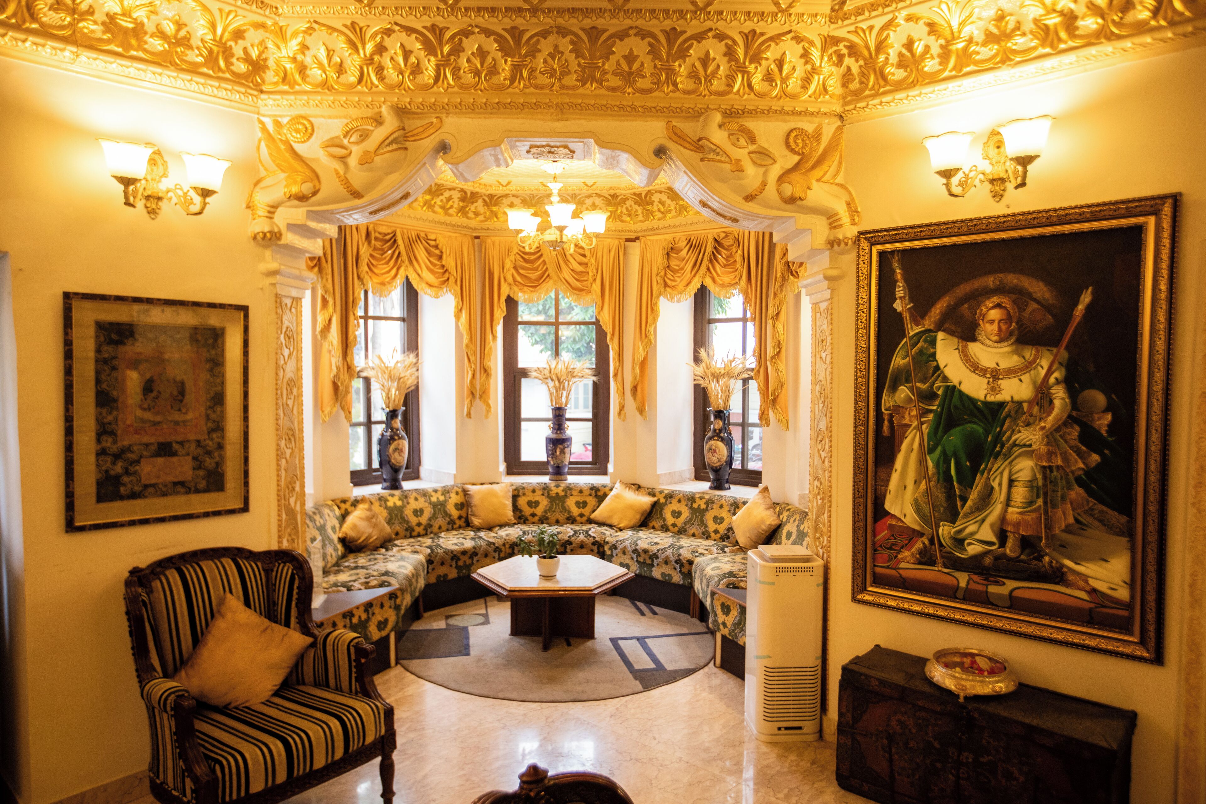 A luxurious room with ornate ceiling decorations, a large painting, a sofa set, and a classic armchair.