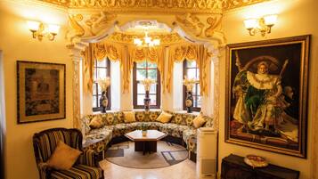 A luxurious room with ornate ceiling decorations, a large painting, a sofa set, and a classic armchair.