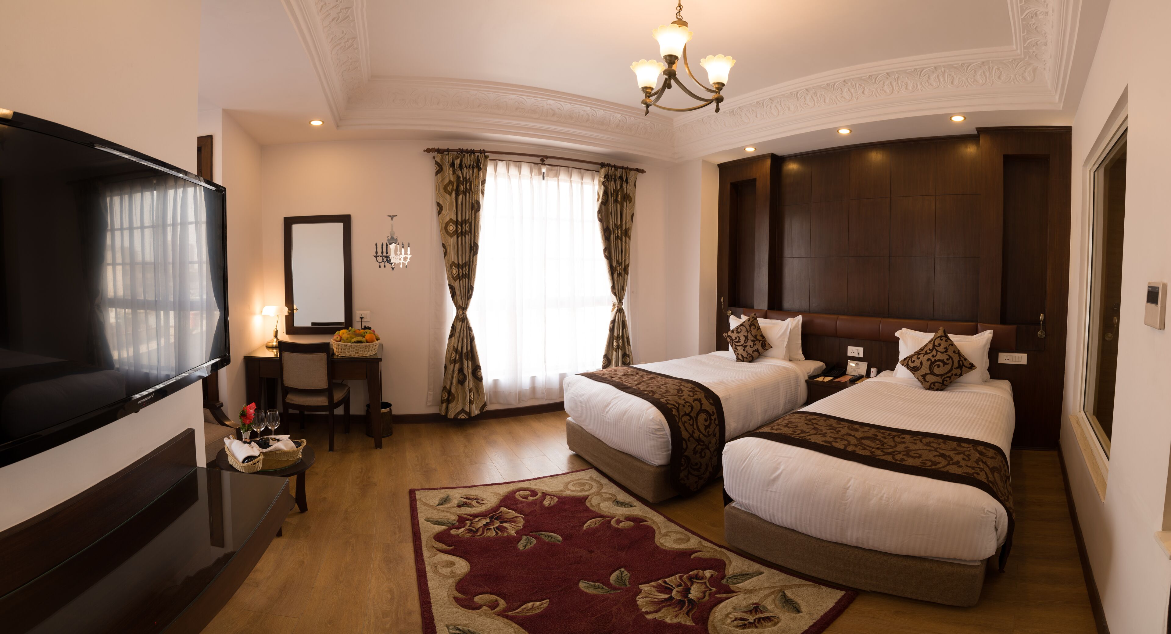 Habitación de hotel con dos camas, televisión, escritorio con lámpara y ventana grande con cortinas.
