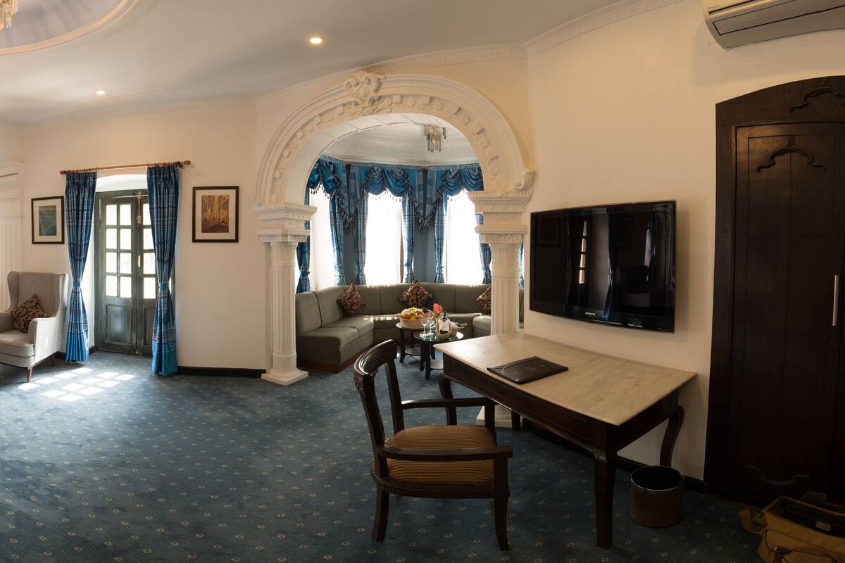 Hotelkamer met een bed, een bank, een bureau, een televisie en een badkamer zichtbaar door een boog.