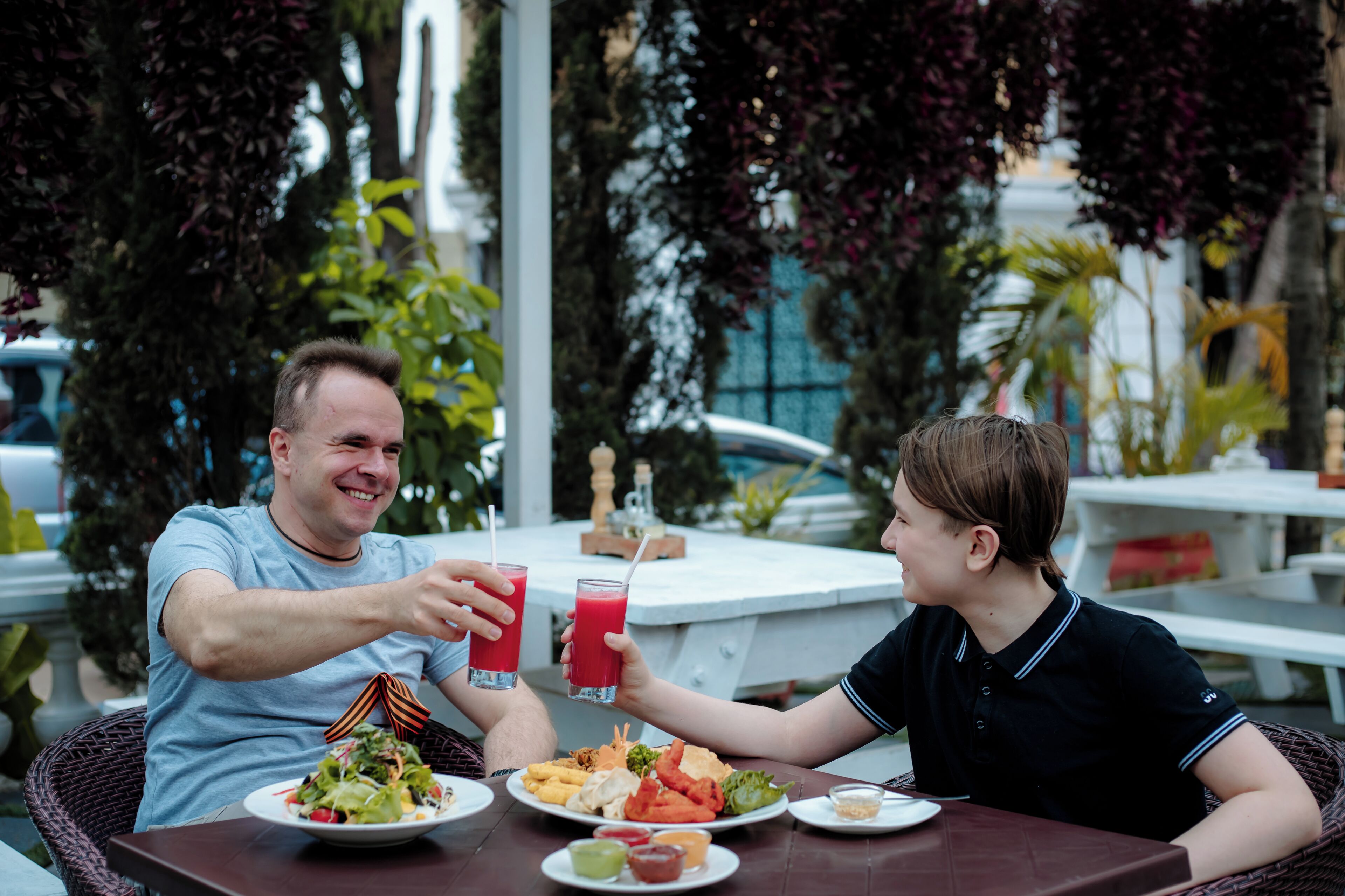 Two people sitting at an outdoor table with plates of food and drinks.