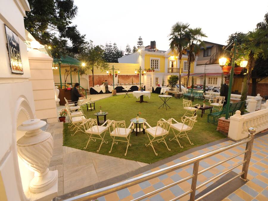 Un patio al aire libre con mesas y sillas, un área con césped y un edificio con balcón.