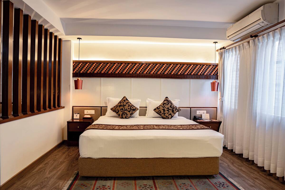 Een keurig ingerichte hotelkamer met een groot bed, houten lambrisering, een gestreept hoofdbord en een decoratief vloerkleed.