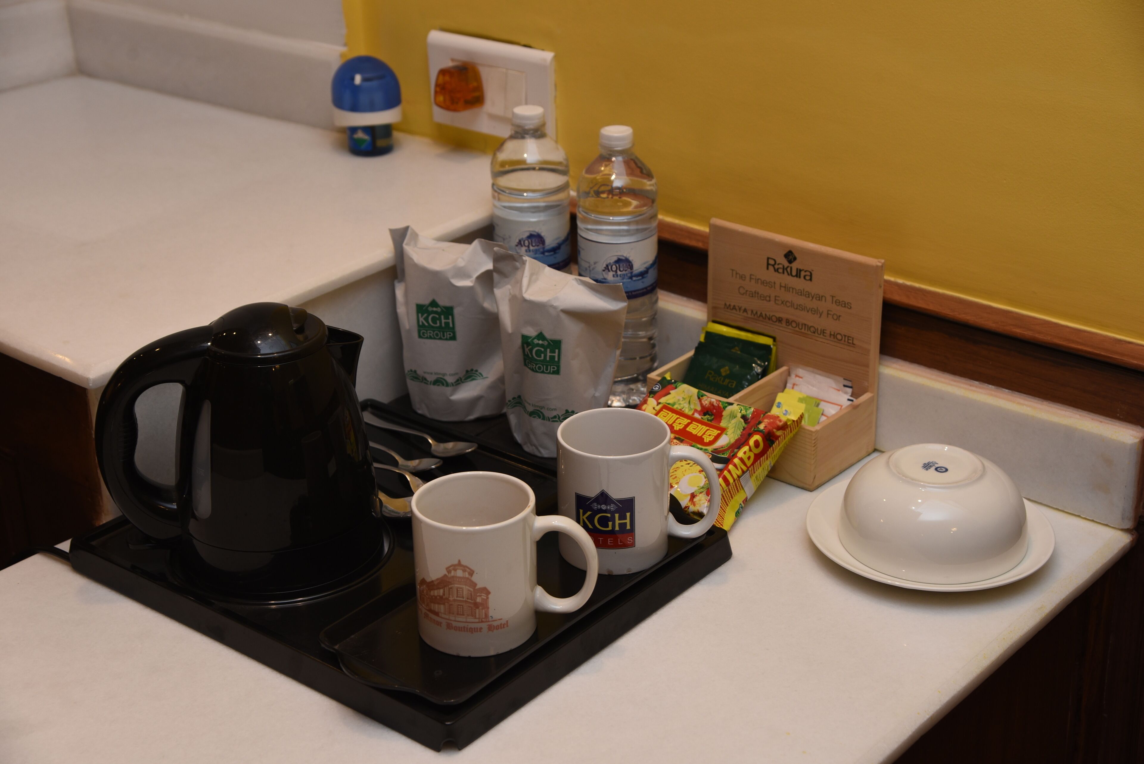 Una bandeja con una cafetera, dos tazas con el logotipo de KGH Group, una tetera blanca y una caja de té.