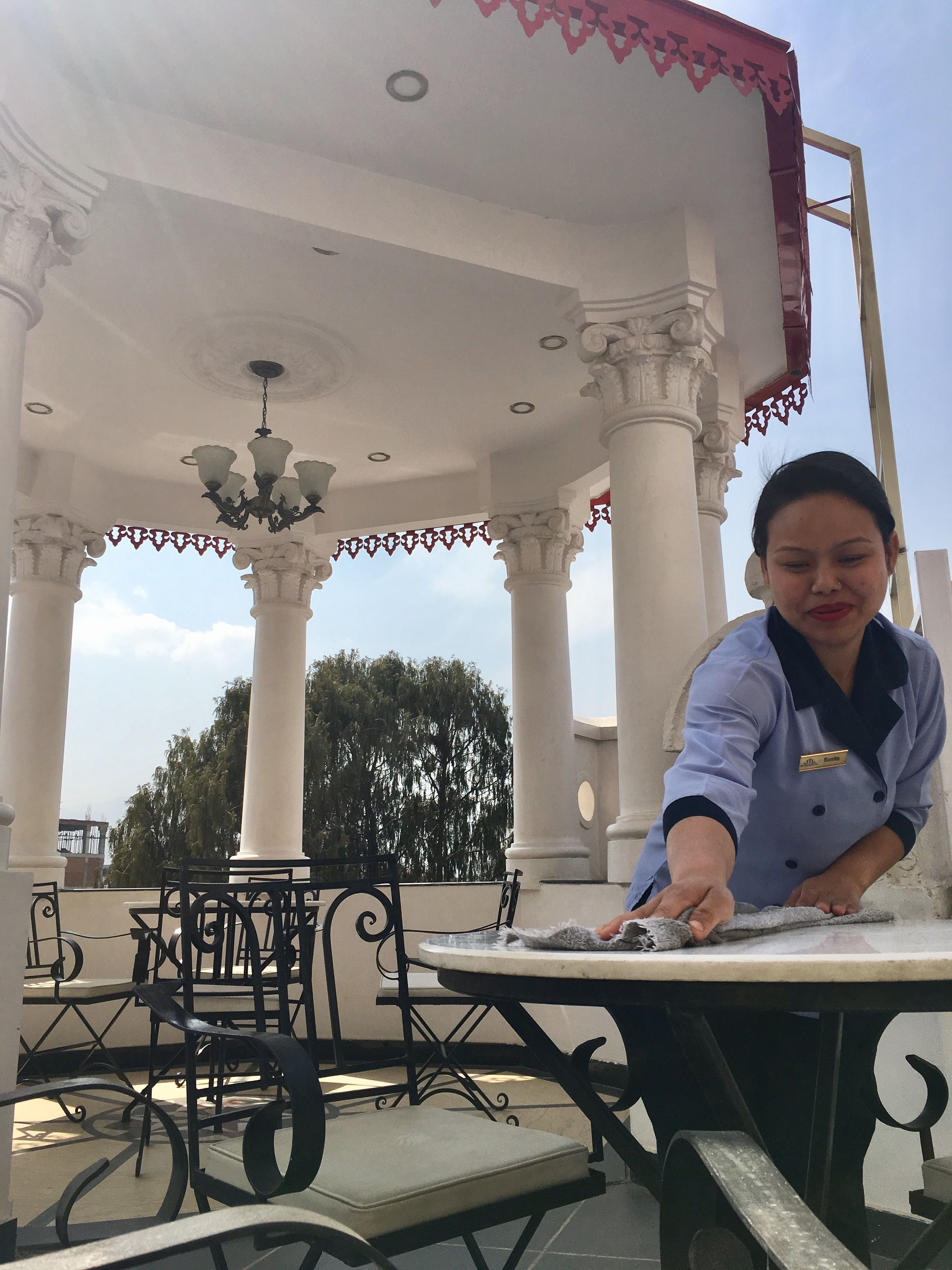 A person cleaning a table in an outdoor area with ornate columns and a chandelier.