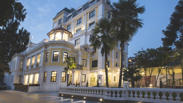 Un imposant bâtiment à plusieurs étages, doté d’une architecture classique, avec un balcon remarquable et une entrée bien éclairée.
