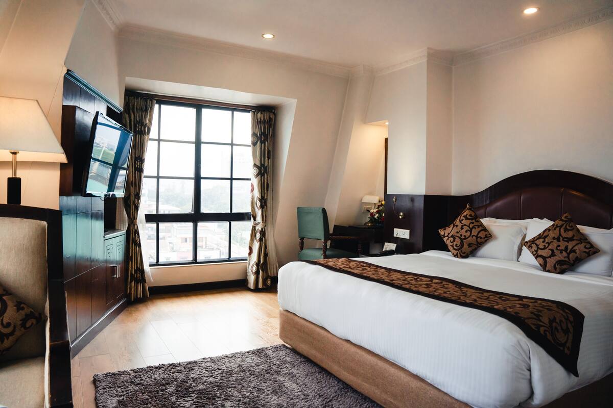 Een hotelkamer met een groot bed, een televisie, een bureau en een raam met gordijnen.