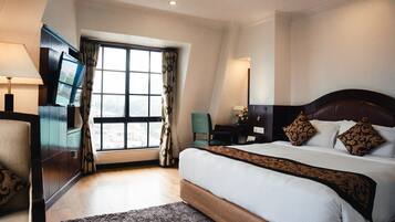Una habitación de hotel con una cama grande, televisión, escritorio y ventana con cortinas.