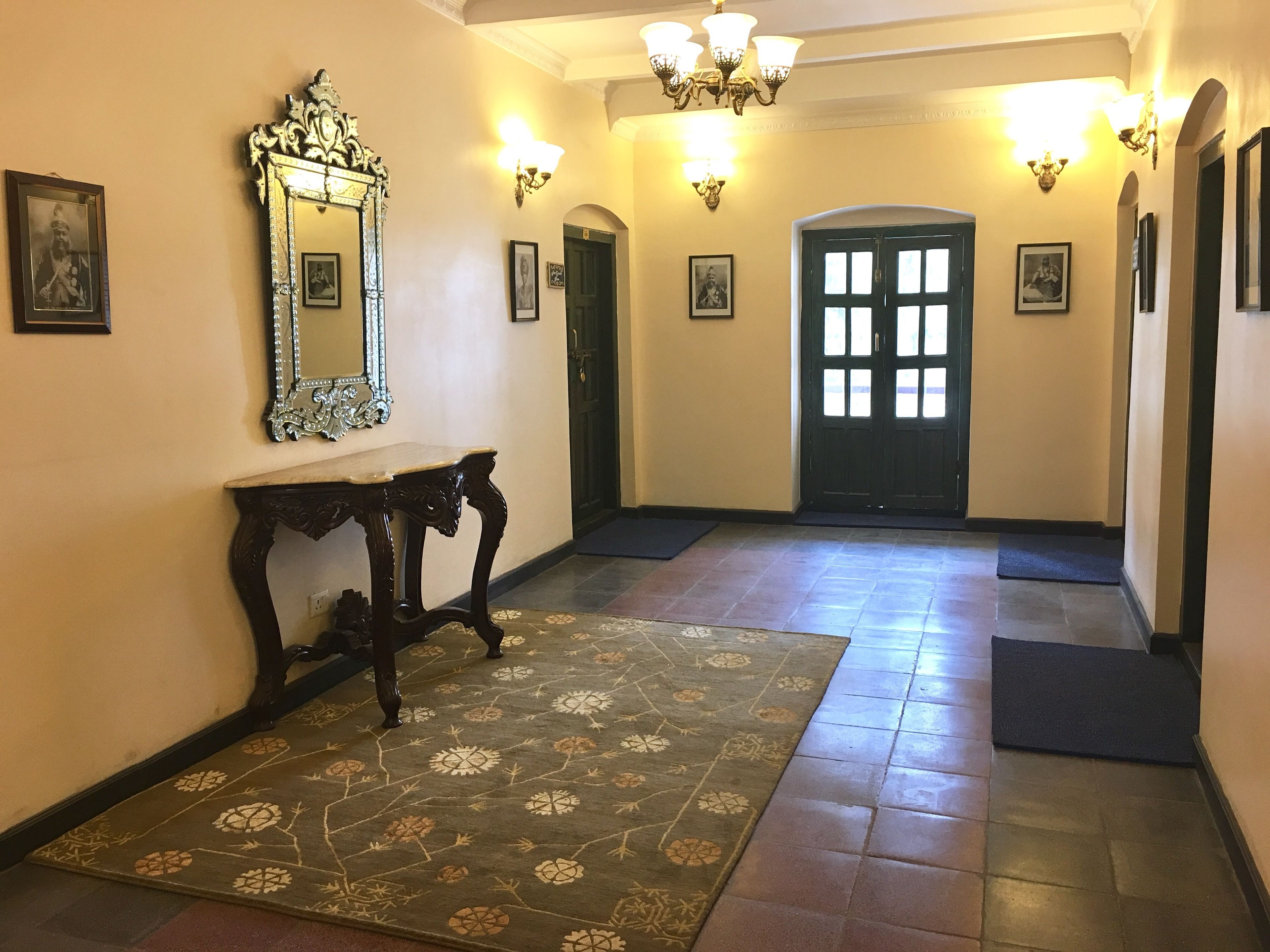 Un pasillo con alfombra estampada, un espejo grande y luces fijadas a la pared.