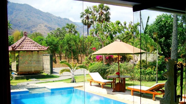 A swimming pool with lounge chairs and a statue, surrounded by lush greenery and a mountain in the background. - Bagus Homestay Pemuteran (Pemuteran)