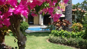A pool area with a clear view of the pool, surrounded by lush greenery and flowering plants. - Bagus Homestay Pemuteran (Pemuteran)