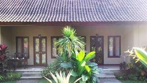 A building with a tiled roof, a covered porch with steps, and a variety of tropical plants. - Bagus Homestay Pemuteran (Pemuteran)
