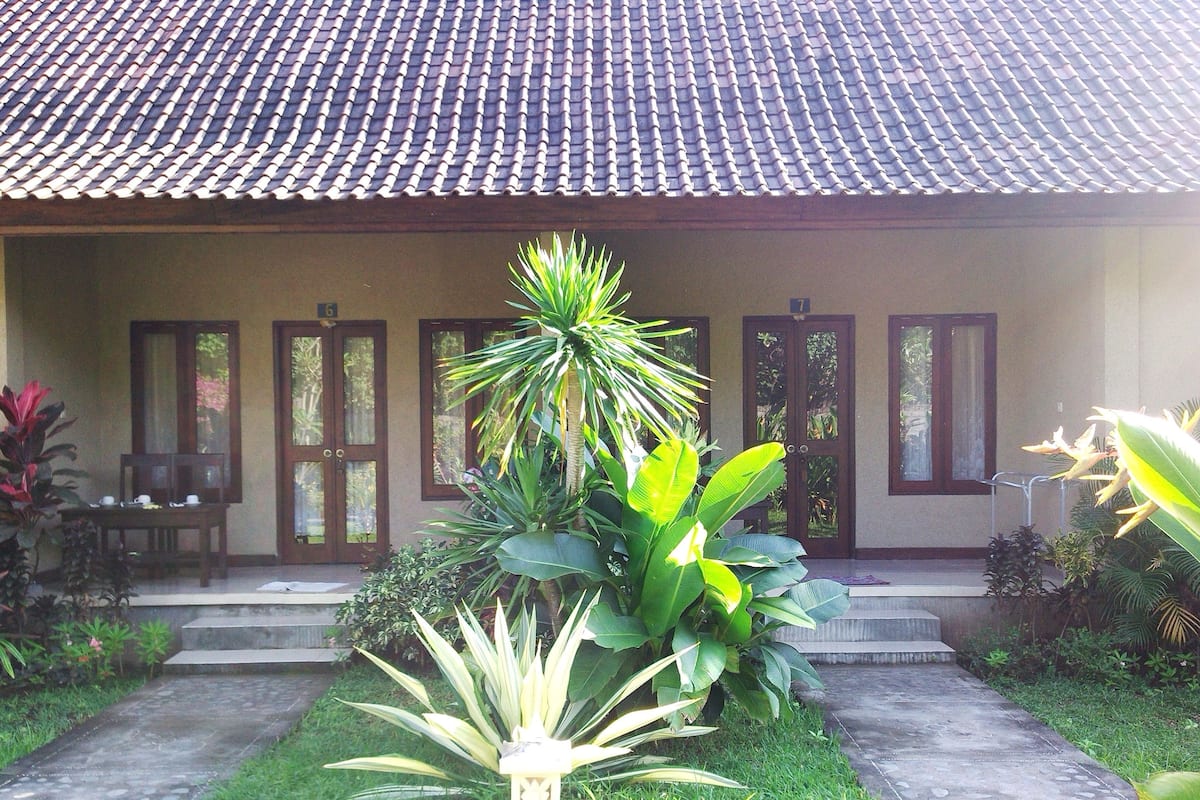 A building with a tiled roof, a covered porch with steps, and a variety of tropical plants.