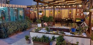 An outdoor patio area with wooden tables and chairs, surrounded by potted plants and a brick wall. - Villa La Lanterna (Pietra Ligure)