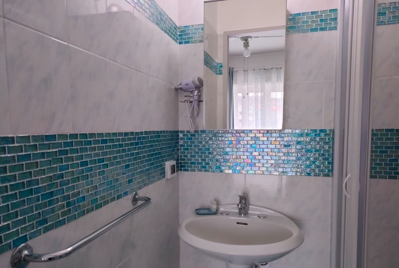 Ein Badezimmer mit gefliestem Boden, einem Waschbecken, einem Spiegel und einer Dusche.