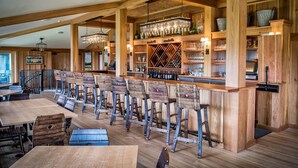 Een rustieke bar met houten barstoelen en planken vol flessen en glazen.