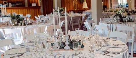 A banquet hall with round tables set for a formal event, featuring white tablecloths, candles, and glassware.