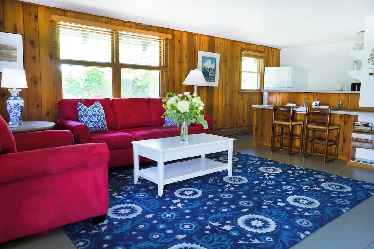 A living room with a red sofa, white coffee table, and a blue patterned rug.