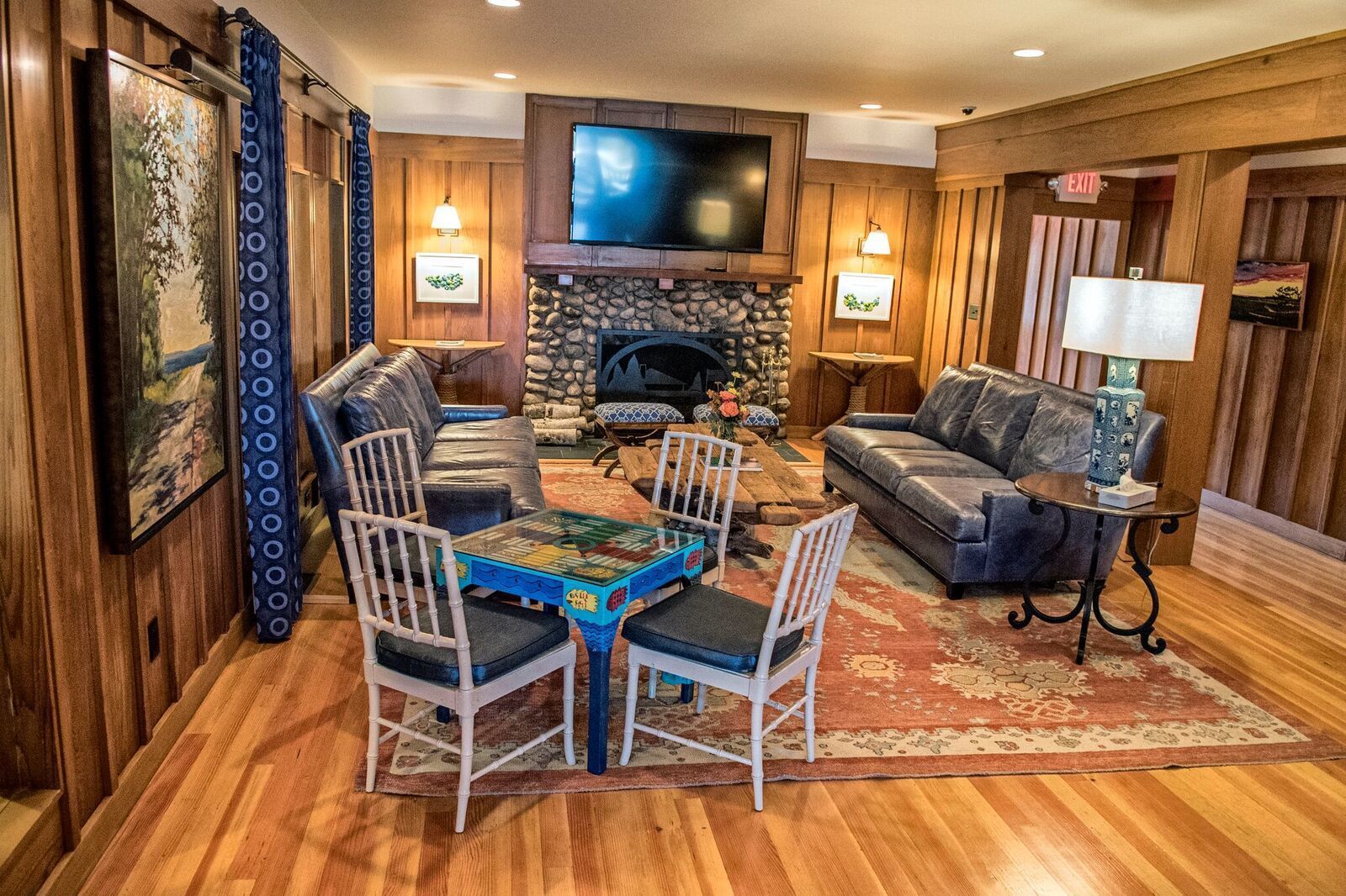 A cozy living room with a stone fireplace, leather sofas, a coffee table, and a TV mounted above the fireplace.