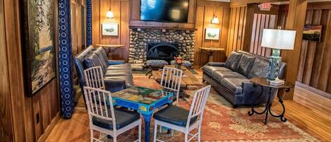 A cozy living room with a stone fireplace, leather sofas, a coffee table, and a TV mounted above the fireplace.