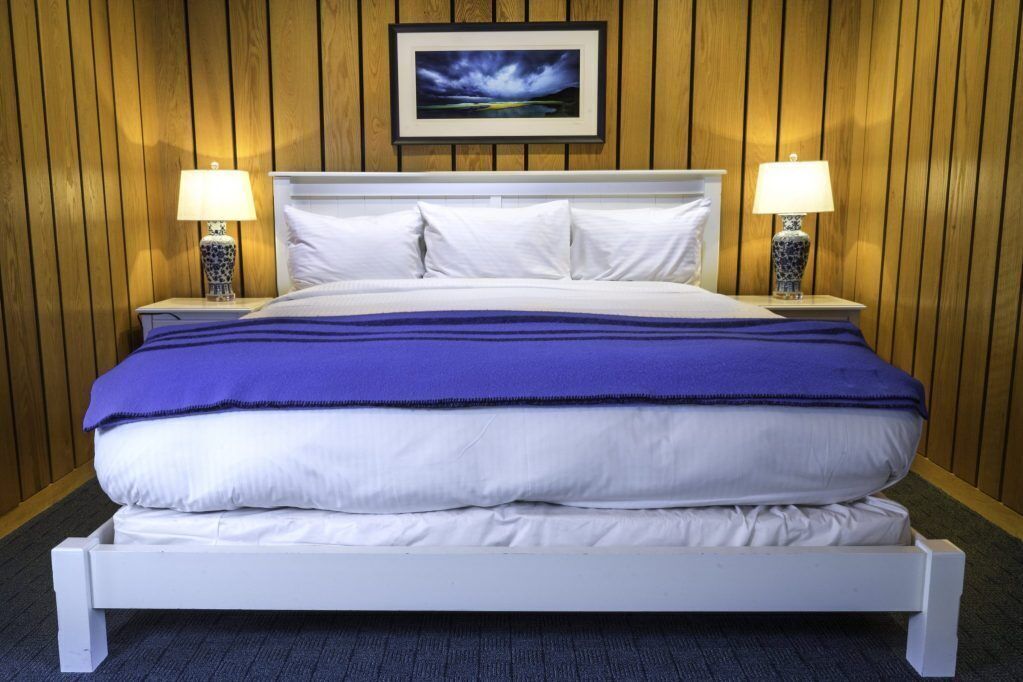 A neatly made bed with white and blue bedding, two bedside lamps, and a framed picture on the wall.